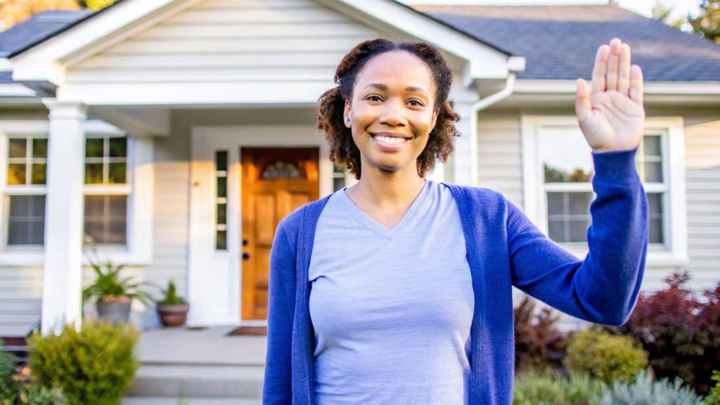 a photo of a happy lady standing in front of her home.